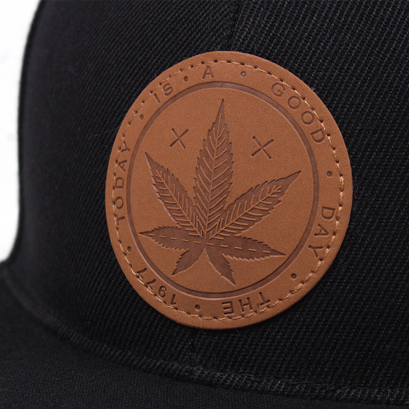 Close-up of a black cap featuring a stylish leather patch with a cannabis leaf design and motivational text.