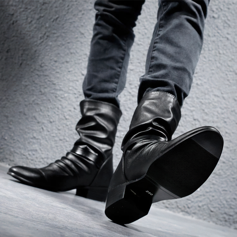 Stylish women's black ankle boots with unique folds, paired with fitted jeans against a textured background.