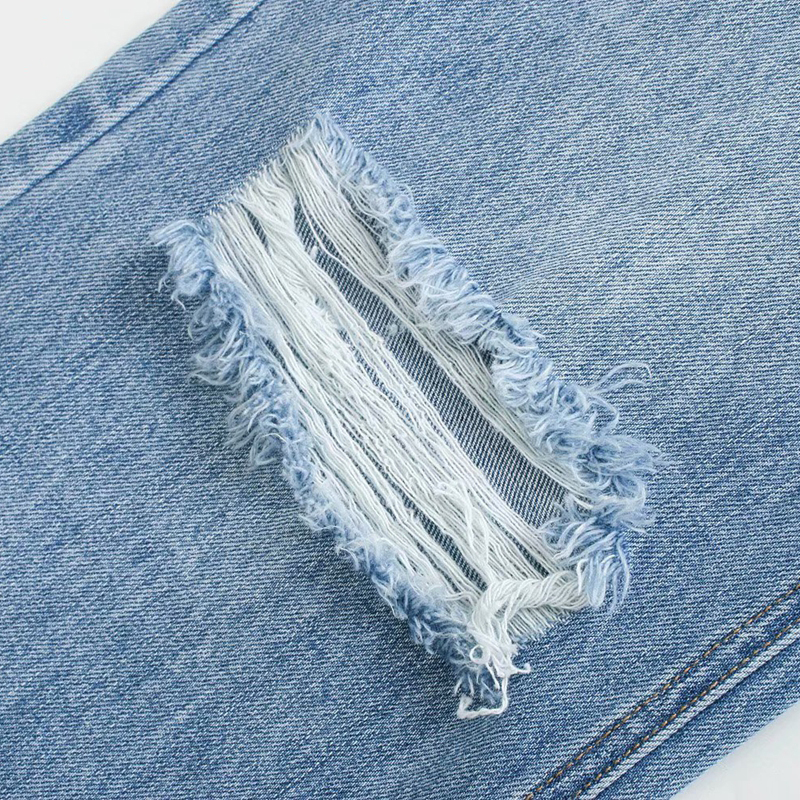 Close-up of ripped detail on high waist wide leg denim jeans, showcasing stylish frayed edges.
