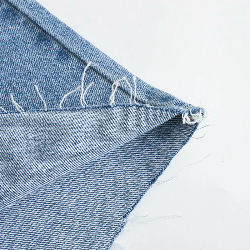 Close-up of frayed edge of wide leg denim fabric showcasing its trendy texture and style.