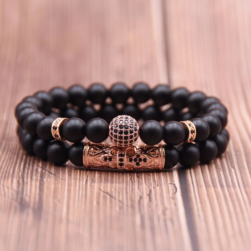 Couple punk style round bracelets with black beads and decorative metallic elements on wooden background.