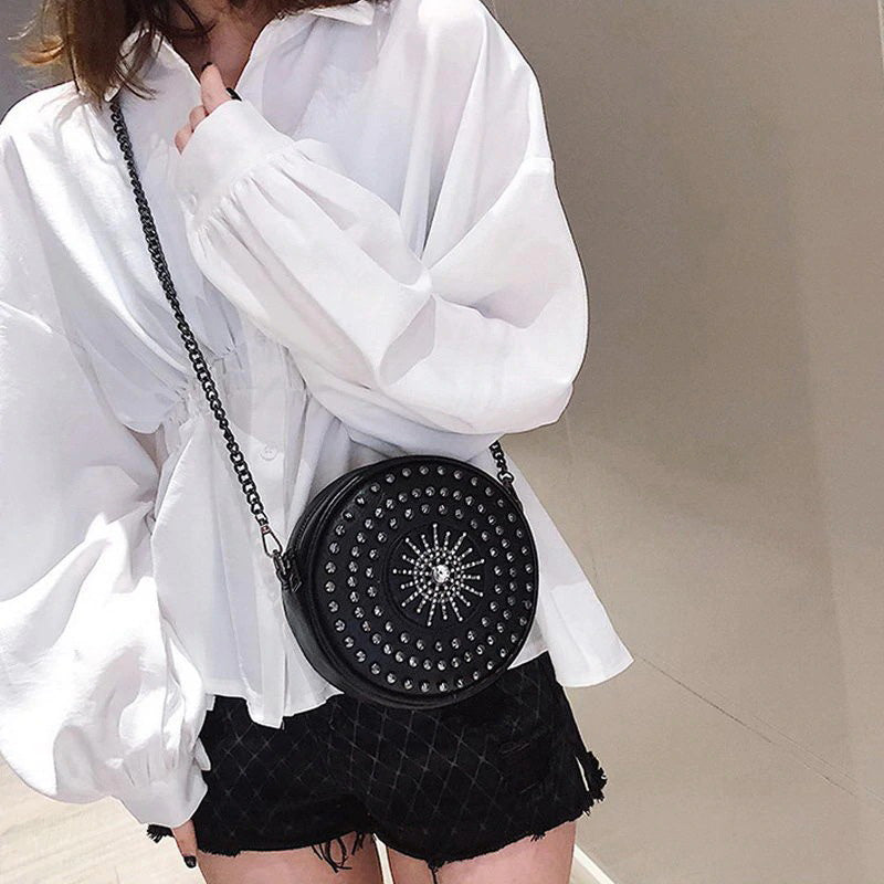 Gothic rock style circular bag for women featuring diamond decor and rivets, paired with a chic white blouse.