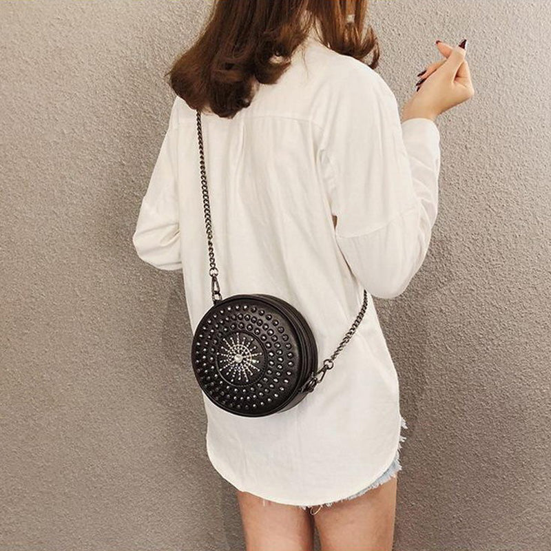 Stylish women's circular bag with diamond accents and rivets, worn as a crossbody. Perfect for a rock-inspired look.