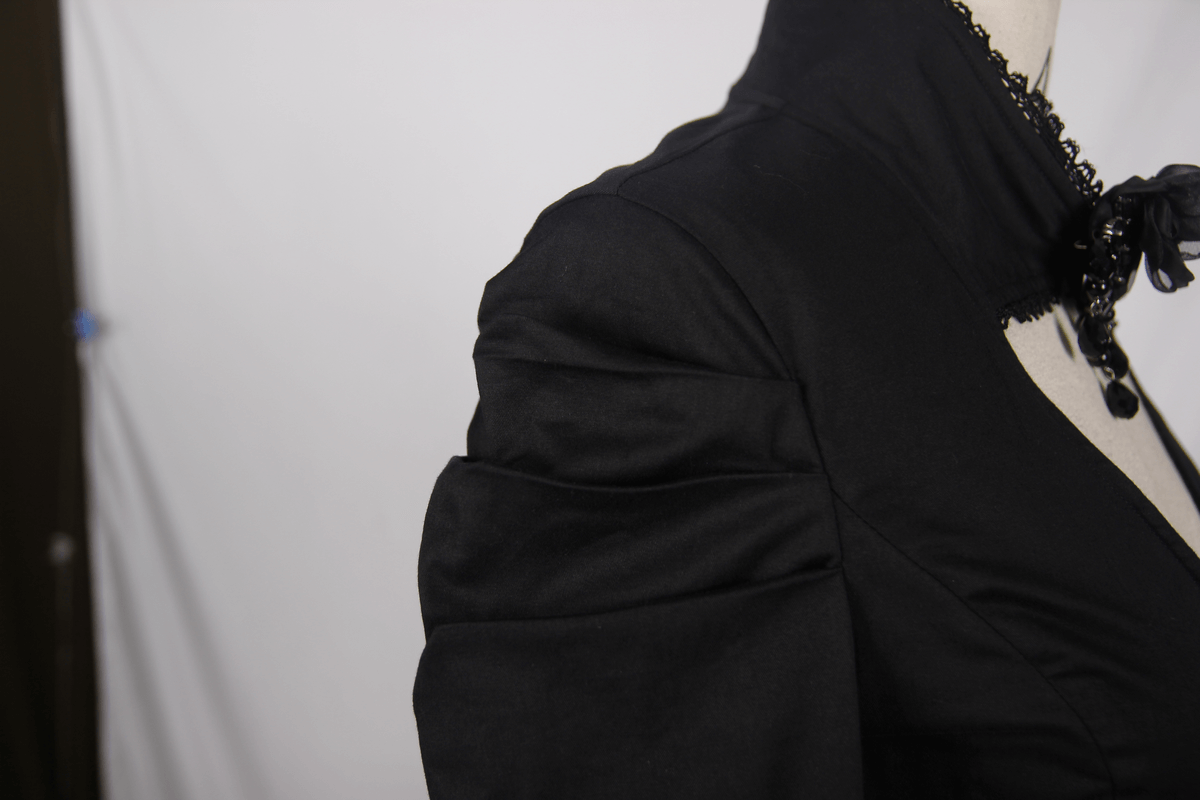 Close-up of an elegant black gothic shirt with stylish puff sleeves and a flower pendant brooch on a mannequin.