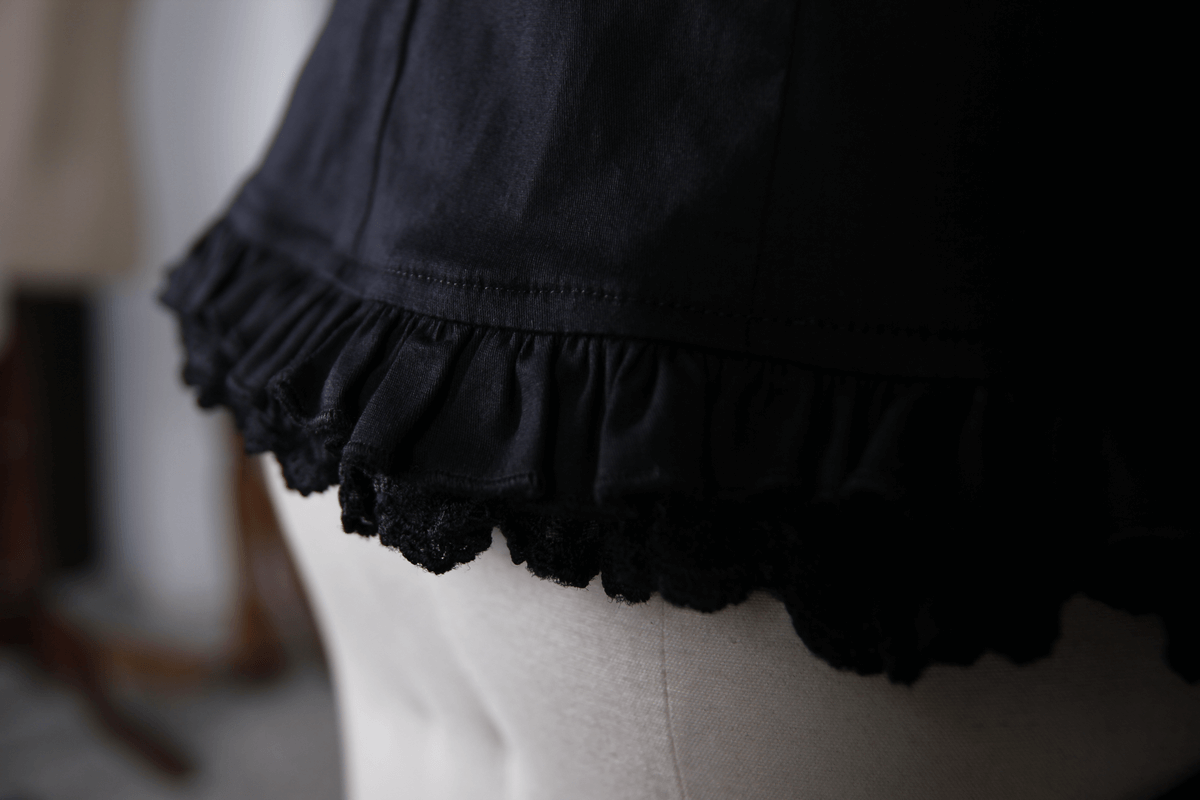 Close-up of the ruffled hem on an elegant black gothic shirt, showcasing intricate lace detailing.