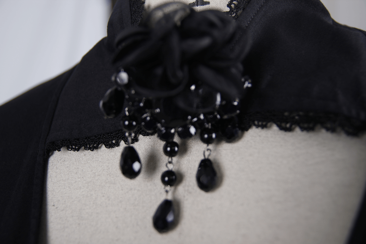 Close-up of an elegant black shirt collar featuring a flower pendant brooch with dangling black beads.