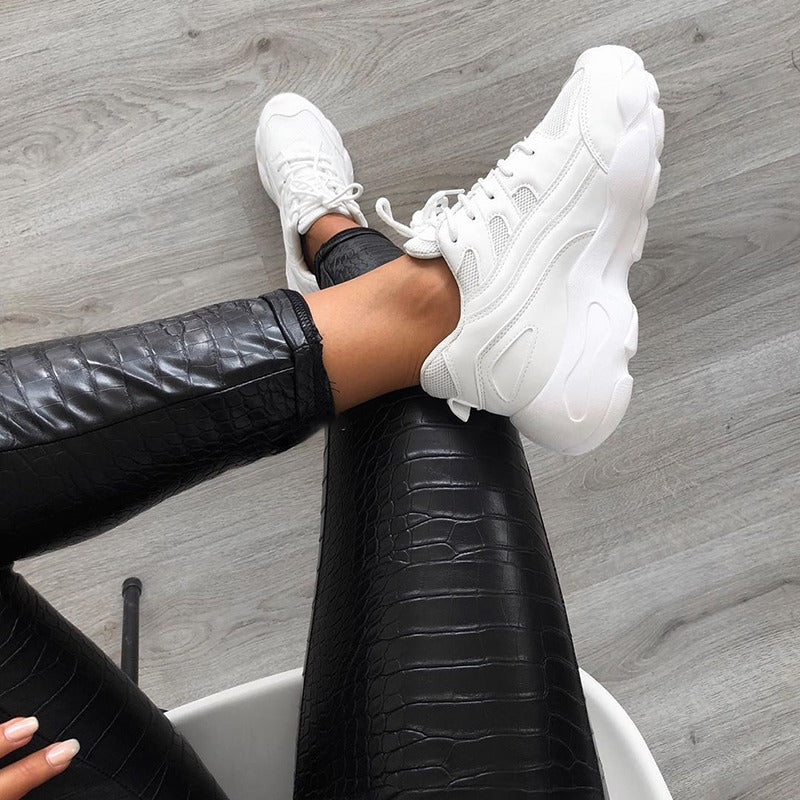 Chic view of woman in high waist faux leather pants and stylish white sneakers, showcasing an edgy rock-inspired outfit.