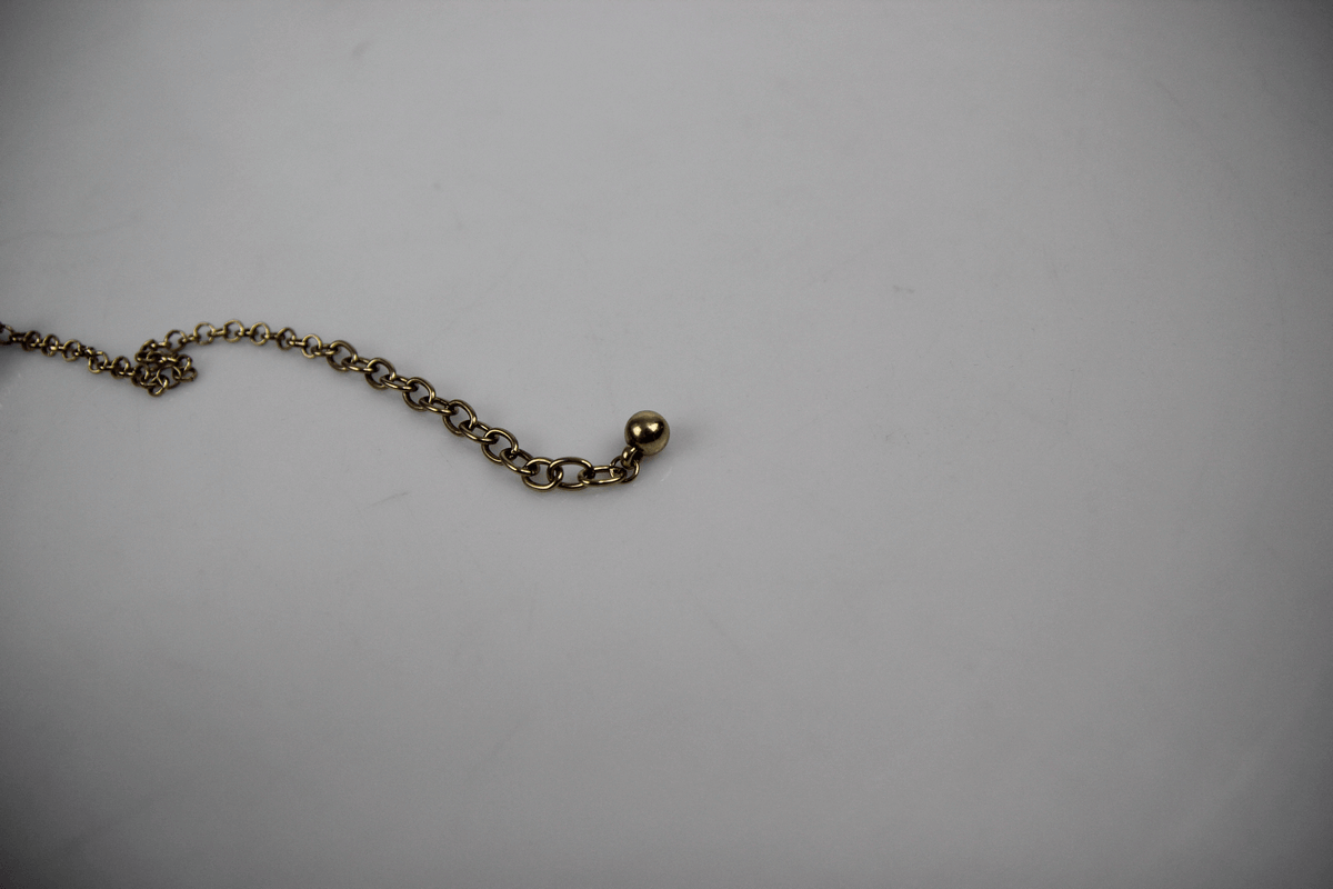 Close-up of a gold necklace chain with a round pendant bead against a light background.