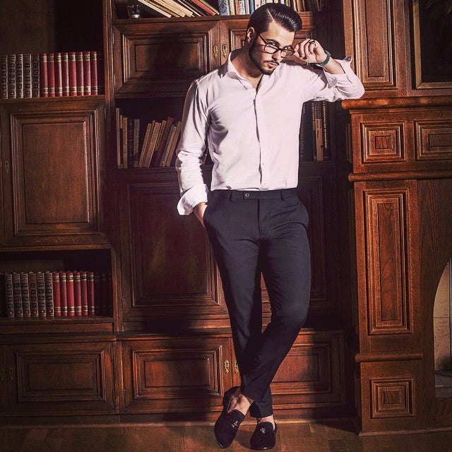 Stylish man in a white shirt and black pants, showcasing exclusive men's skull buckle loafers in a cozy library setting.
