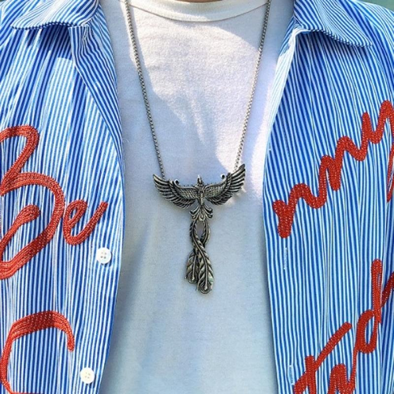 Vintage stainless steel phoenix pendant with open wings worn over a white shirt and striped blue shirt.