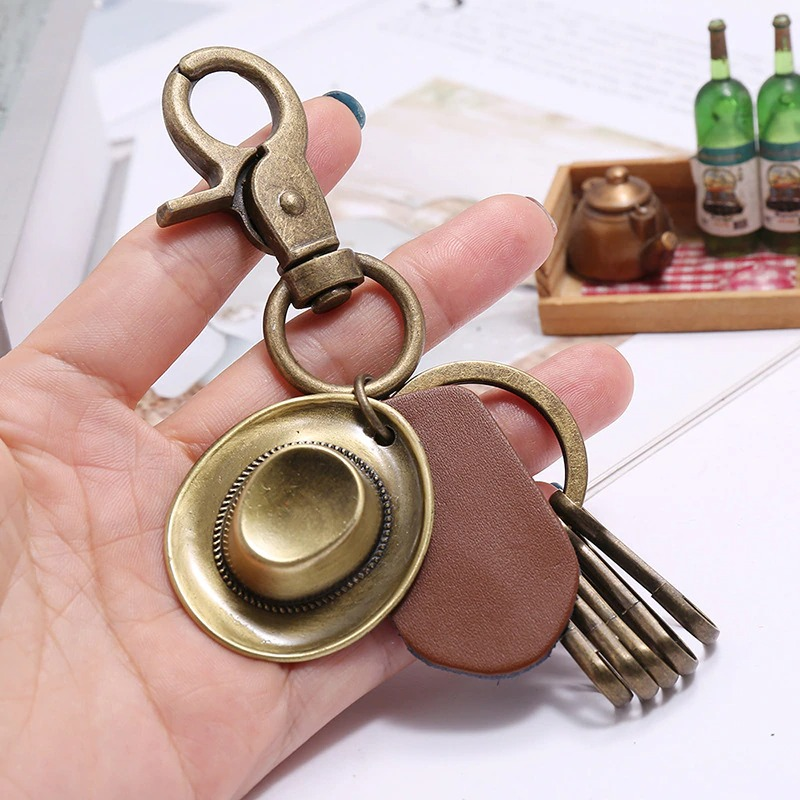 Vintage alloy keychain with hat pendant and leather detail, perfect accessory for car lovers.