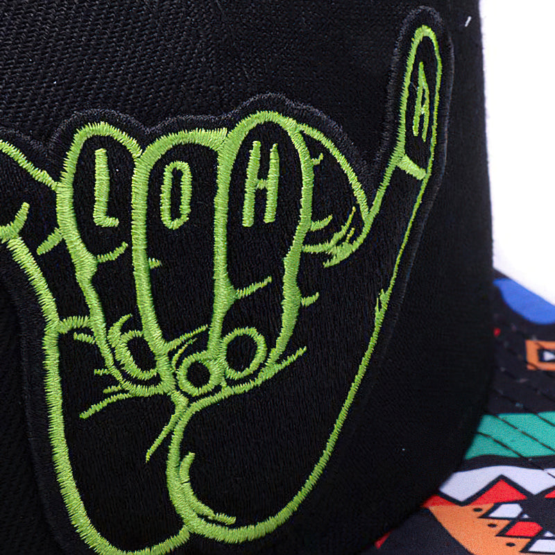 Close-up of a black alternative style cap featuring a vibrant green 'Aloha' hand sign embroidered design.