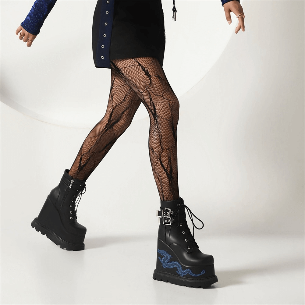 Model showcasing stylish black dragon embroidered wedge boots paired with fishnet tights and a trendy skirt.