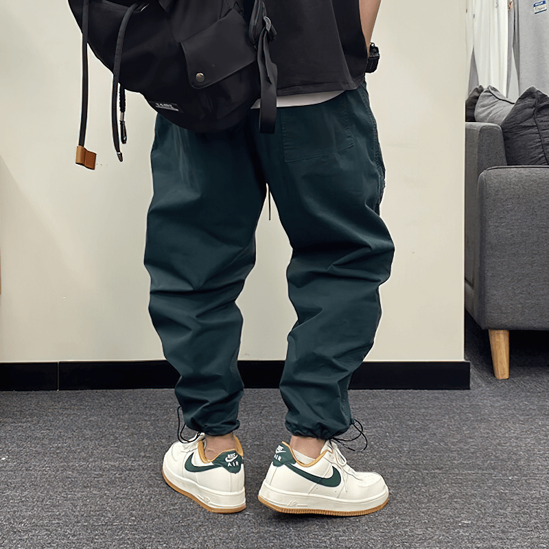 Casual drawstring harem pants in dark green, styled with white sneakers and a black backpack.