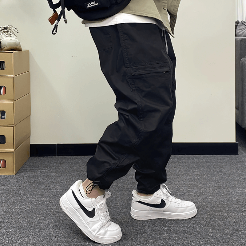 Casual black drawstring harem pants paired with white sneakers, showcasing a modern cargo style in a trendy setting.