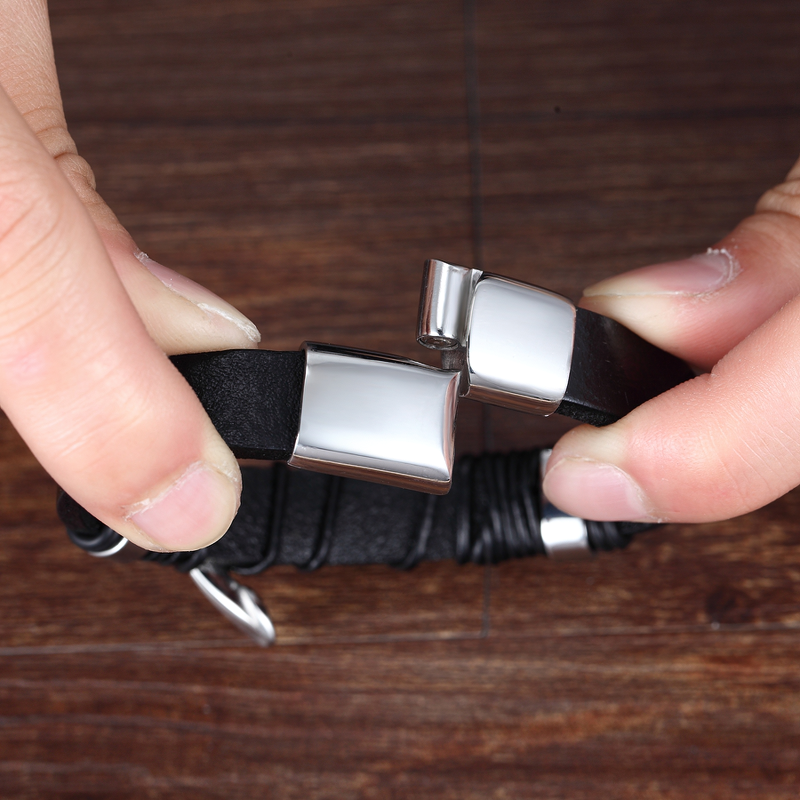 Close-up of hands holding a stainless steel and leather bracelet with feather, showcasing its trendy design.