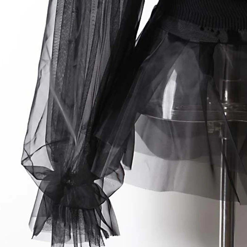 Close-up of the sheer black long sleeves and tulle hem of a gothic style turtleneck dress-like sweater.