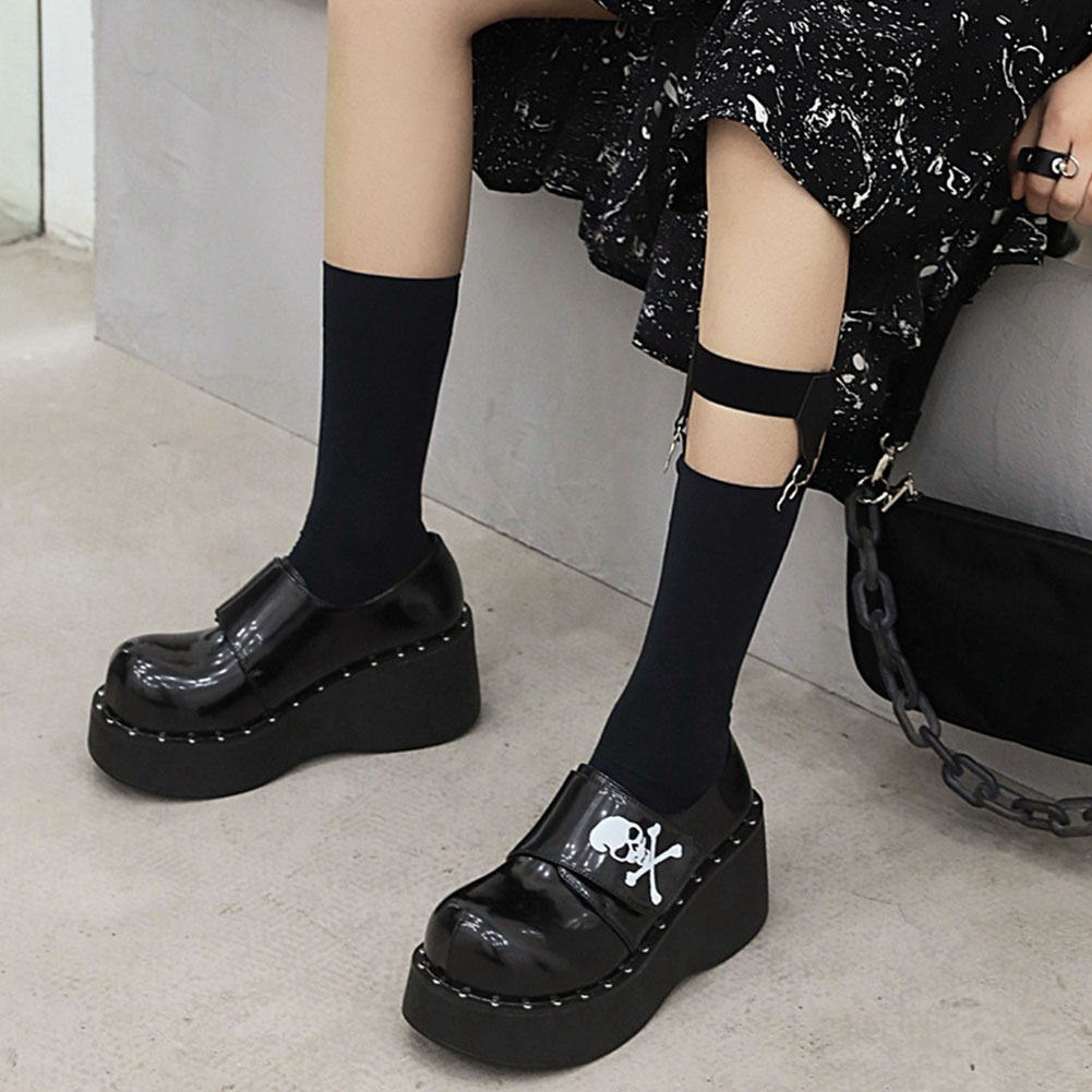 Gothic women's platform shoes in patent leather, featuring a skull design, paired with stylish black socks and a casual outfit.