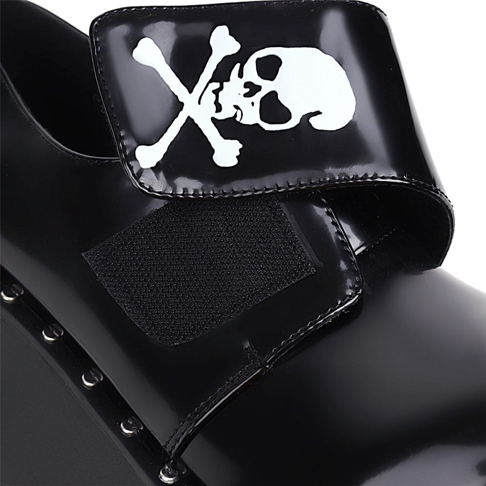 Close-up of Gothic platform shoes with a skull and crossbones velcro strap, showcasing black patent leather details.