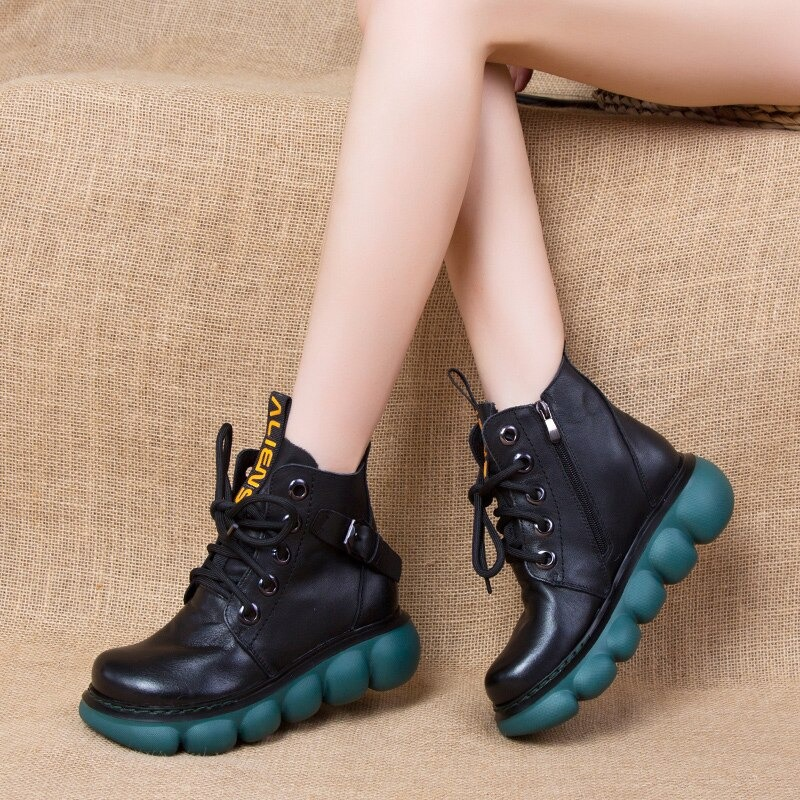 Trendy women's black genuine leather ankle boots with thick teal platform sole on a textured background.