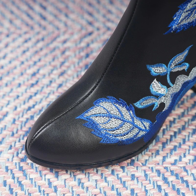 Close-up of fashion ladies genuine leather ankle boot with blue embroidered floral design on black leather.