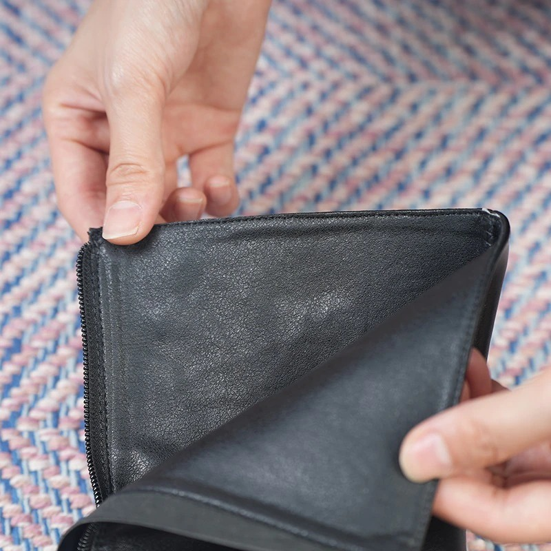 Close-up of hands opening a black leather wallet, showcasing its interior details on a colorful woven background.