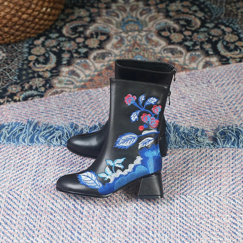Black ethnic style leather ankle boots with floral embroidery and square heels on patterned fabric.