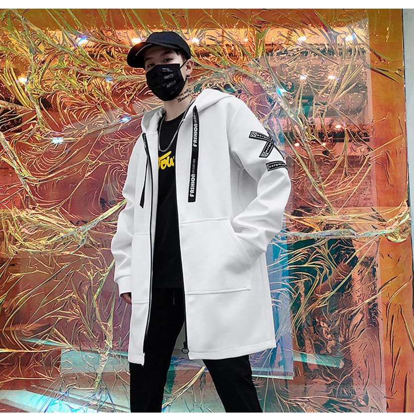 Stylish man in a white long coat with hood, showcasing casual fashion against an artistic background.