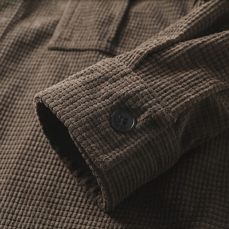 Close-up of brown oversized male shirt sleeve with textured fabric and button detail, showcasing alternative style.