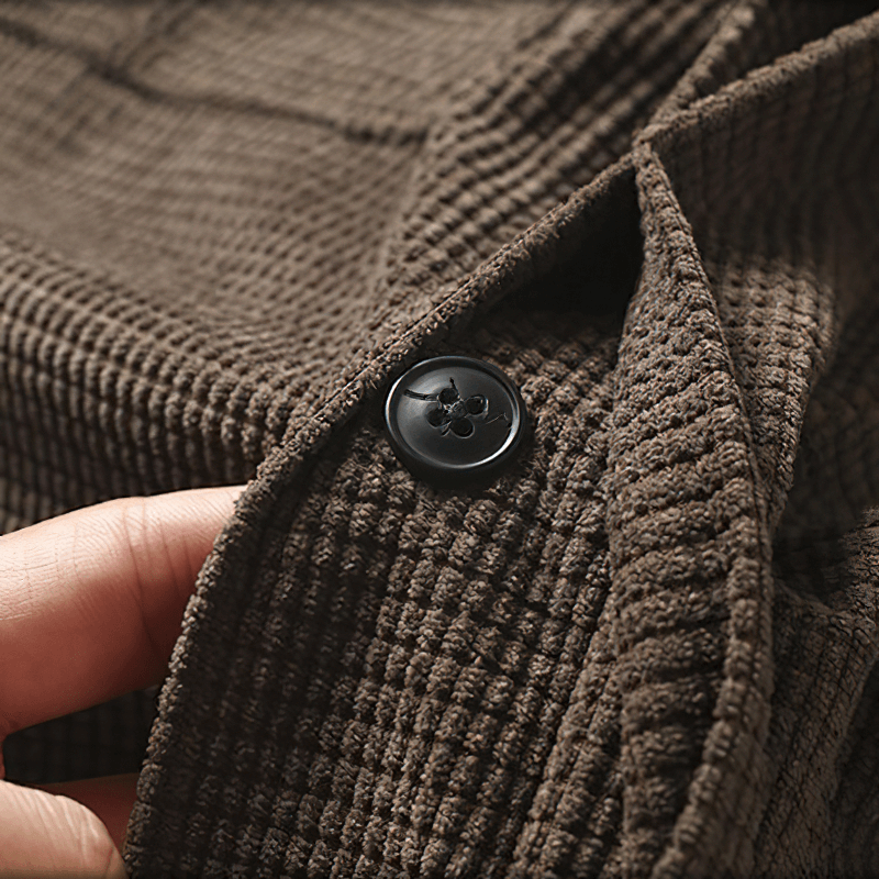 Close-up of a men's oversized shirt showing a brown textured fabric and a black button detail.