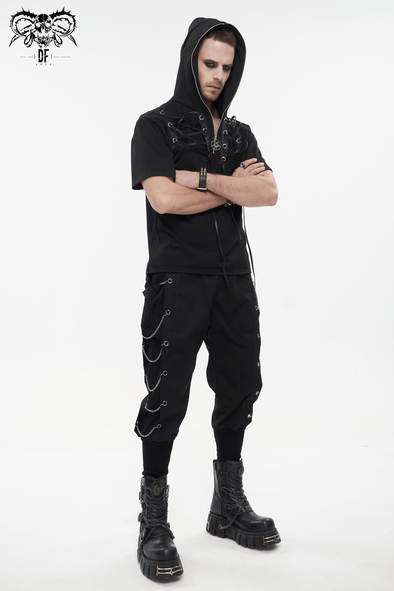 Stylish man in black gothic punk outfit, featuring loose cargo pants with chain eyelets and a hooded top.