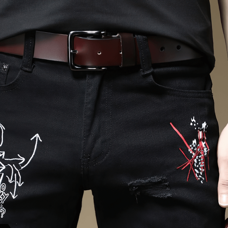Close-up of stylish men's black slim jeans with creative prints and a brown belt, perfect for casual wear.