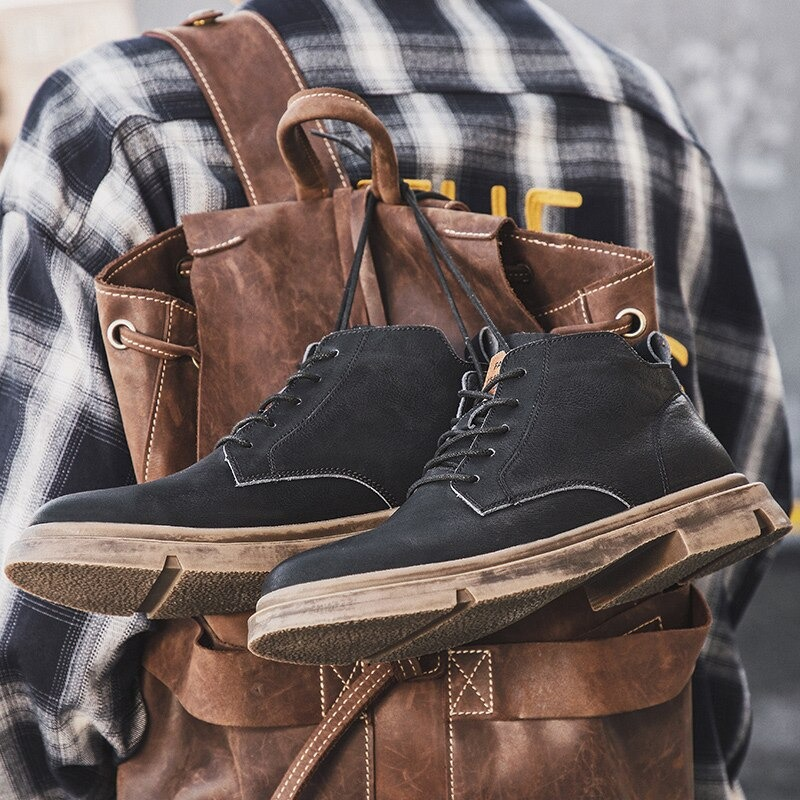 Stylish men's ankle leather boots in casual British style, featuring a rubber sole, hanging from a backpack.