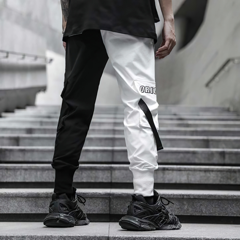 Men's black and white patchwork cargo pants on stairs, showcasing stylish casual trousers with pockets.