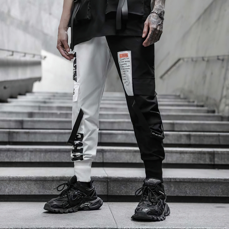 Men's black and white patchwork cargo pants with pockets, styled for an edgy casual look on urban stairs.