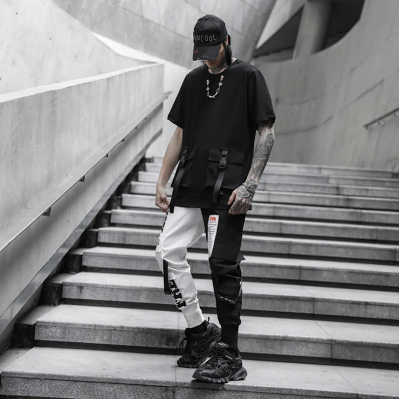 Stylish man wearing black and white patchwork cargo pants and a black t-shirt on stairs, showcasing casual streetwear fashion.