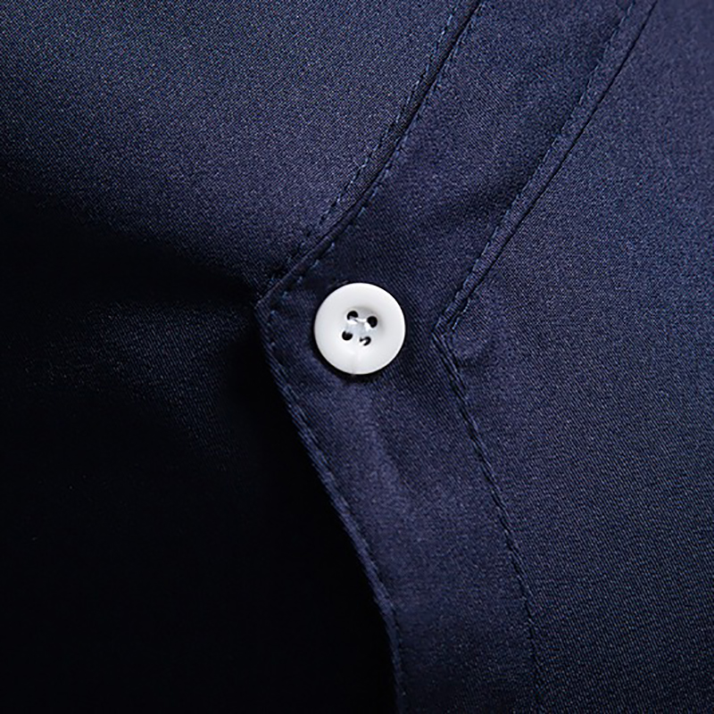 Close-up of a white button on a navy blue men's asymmetric shirt showcasing fine cotton fabric.
