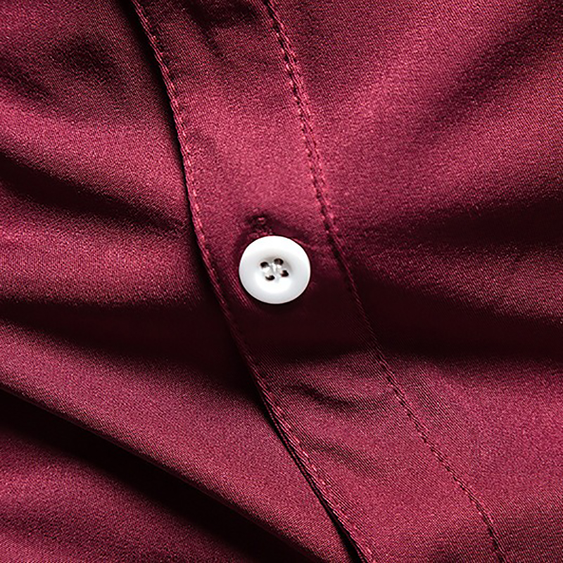 Close-up of a white button on a stylish men's maroon asymmetric shirt, showcasing quality cotton fabric.