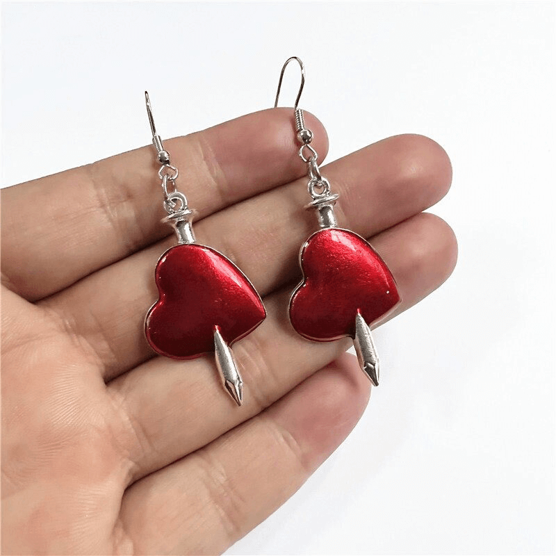 Fashionable red heart earrings with gothic arrow design, hanging elegantly from a model's hand.