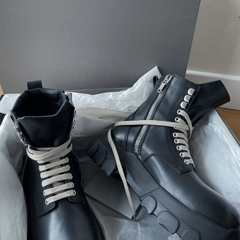 Stylish black thick-sole ankle boots with light-colored laces, showcased in a shoe box.