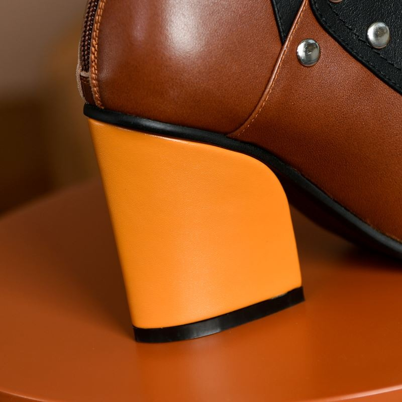 Close-up of a stylish brown leather ankle boot with an orange high heel, showcasing its unique design and rivet details.