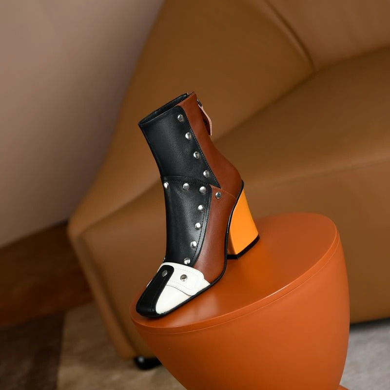 Fashionable women's high heel ankle boots in multicolour leather with rivets, showcased on a stylish chair.