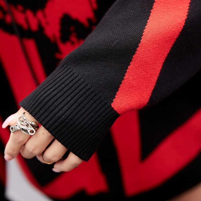 Close-up of a hand in a women's oversized knitting hoody showcasing a stylish black and red design with a skull print.