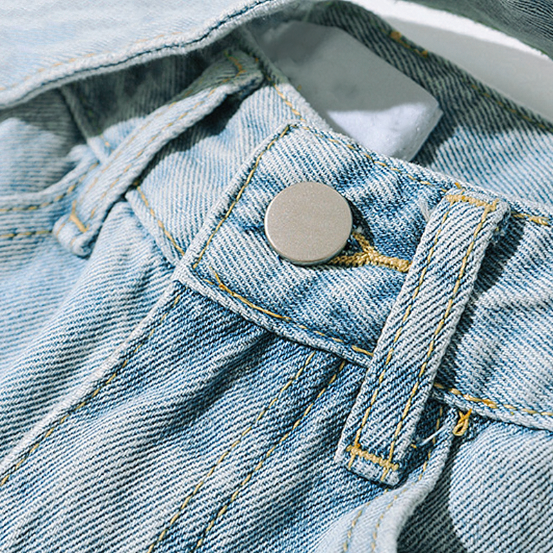 Close-up of the button and waistband of trendy loose denim jeans with belt pockets and soft fabric.