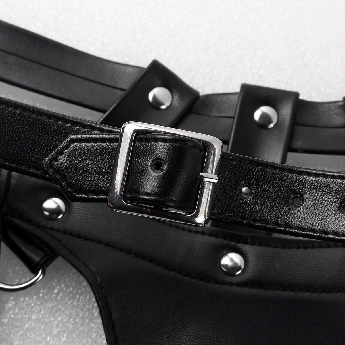 Close-up of a black faux leather body chest harness featuring adjustable buckle and metallic studs for a stylish punk look.