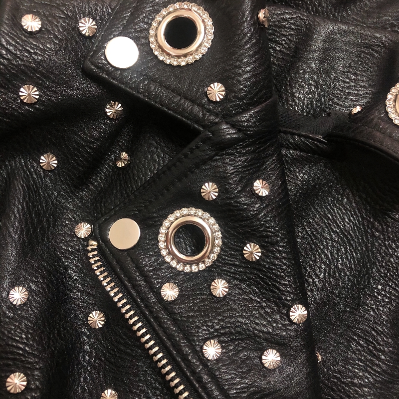 Close-up of a black faux leather women’s jacket adorned with silver rivets, showcasing a rock style aesthetic.