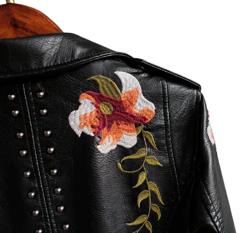 Close-up of floral embroidery on faux leather women's motorcycle jacket with silver studs.
