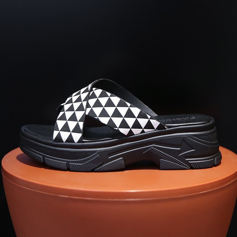 Stylish black and white alternative style sandals with geometric design on a pedestal.
