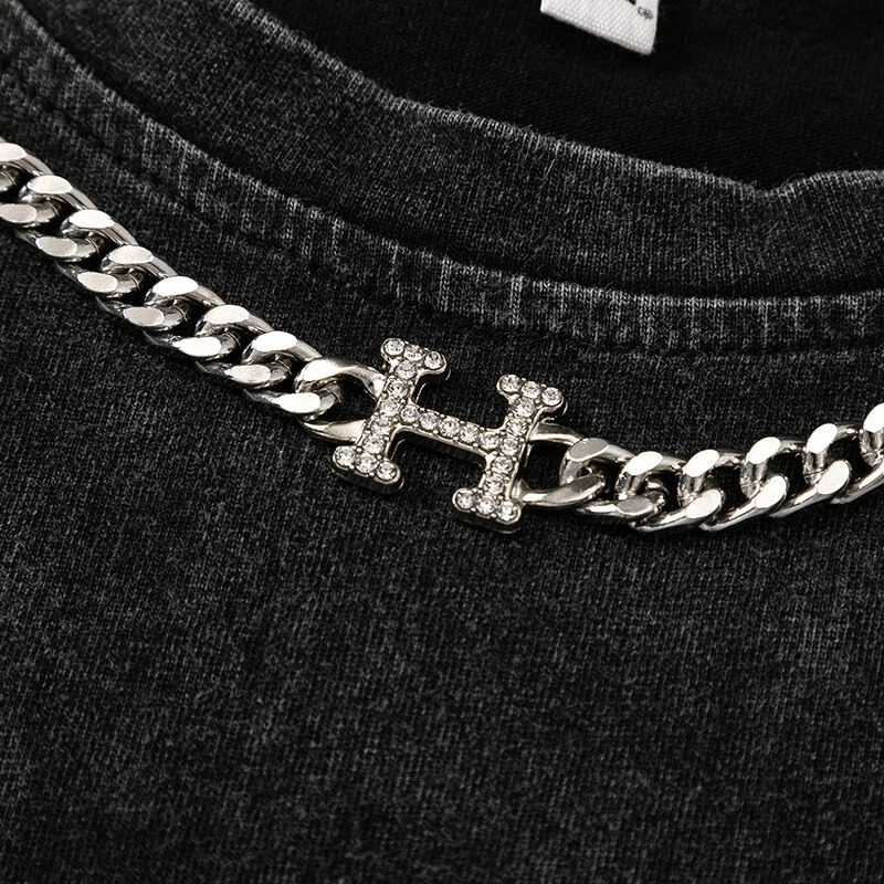 Close-up of a stylish silver chain necklace with a rhinestone 'H' on a black tank top, perfect for gothic fashion.