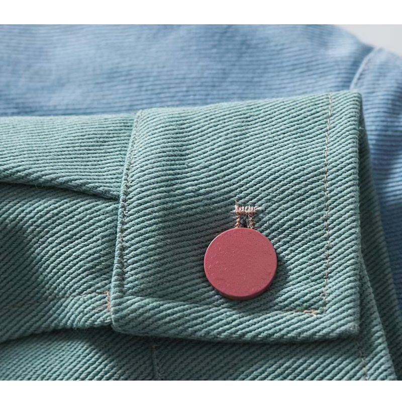 Close-up of a green fabric jacket cuff with a stylish round pink button detail.